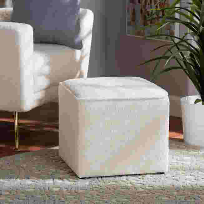 Ivory boucle upholstered ottoman in a living room setting with a white armchair and plant